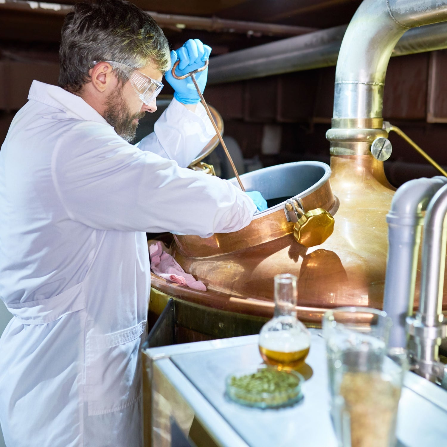 Profile view of brewer wearing white coat and protective gloves controlling process of beer fermentation